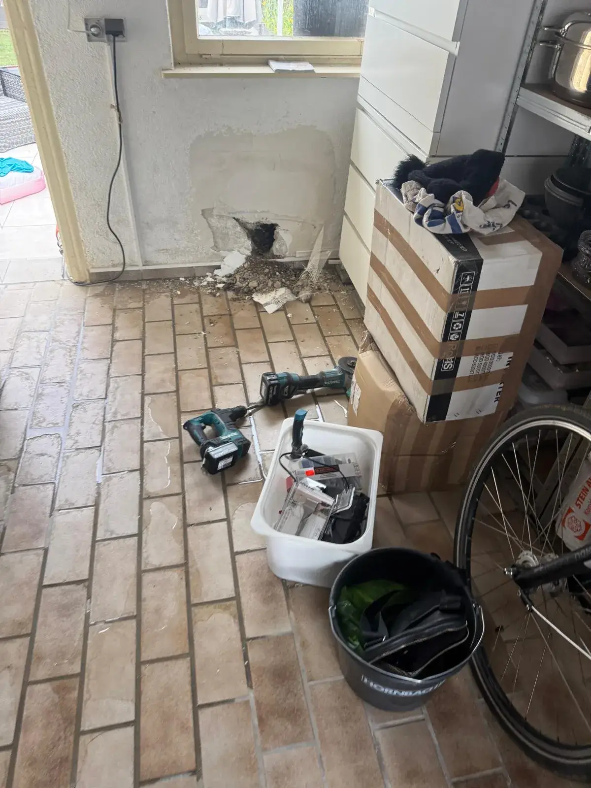 Arbeitsstelle nach Leckortung mit Werkzeug, geöffneter Wand und Feuchtigkeit auf dem Fliesenboden